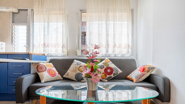 Uma sala de estar com sofá, mesa de centro de vidro e um vaso com flores.