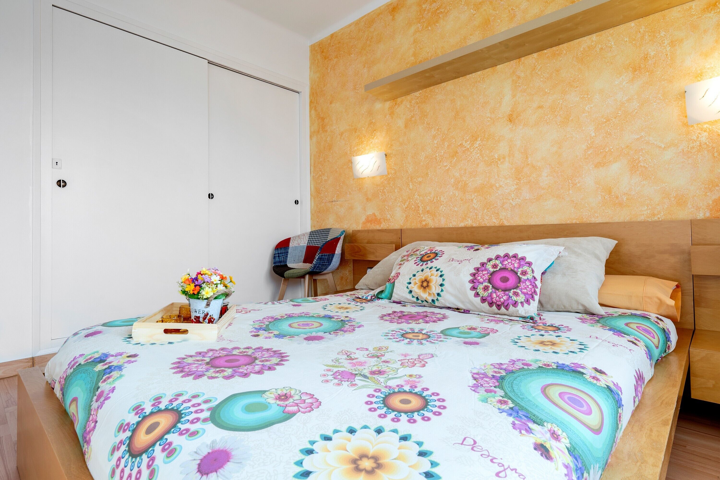 Un dormitorio con cama, mesita de noche, silla, lámpara de pared y cabecero de madera.