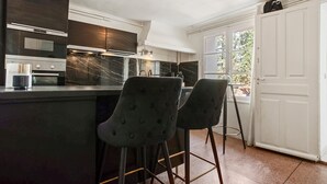 Eine Küche mit dunklen Schränken, einer Marmor-Spritzschutzwand, einem eingebauten Backofen und zwei Barhocker.