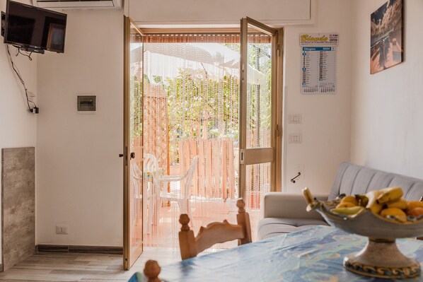 A room with a bed, a table with a fruit bowl, a TV mounted on the wall, and a calendar on the wall.