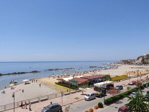 A beachside view with a paved walkway, beach umbrellas, and a row of buildings along the shore.