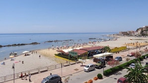 Blick auf einen Strand mit einem gepflasterten Weg, Strandpalmen und einer Reihe von Gebäuden entlang der Küste.