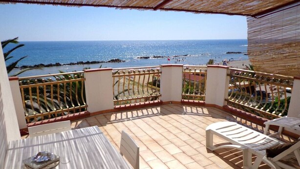 A balcony with a view of the sea, a table, and two chairs.