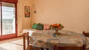 A dining area with a table set for two, a chair, a floor lamp, and a window with blinds.