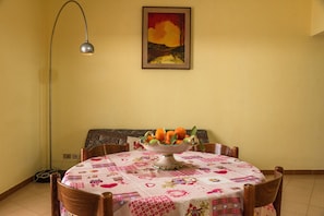Une table à manger avec un panier de fruits, une nappe à motifs et un tableau accroché au mur.