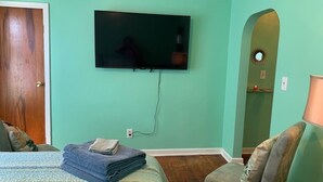 A bedroom with a bed, a television mounted on the wall, a chair, and a folded towel on the bed. - Beach Side Studio #4 - Pet Friendly, WiFi, Off-Street Parking, Large Smart TV (Norfolk)