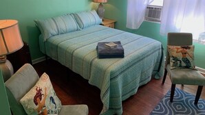 A bedroom with a bed, a chair, a nightstand, a lamp, and a window with curtains. - Beach Side Studio #4 - Pet Friendly, WiFi, Off-Street Parking, Large Smart TV (Norfolk)