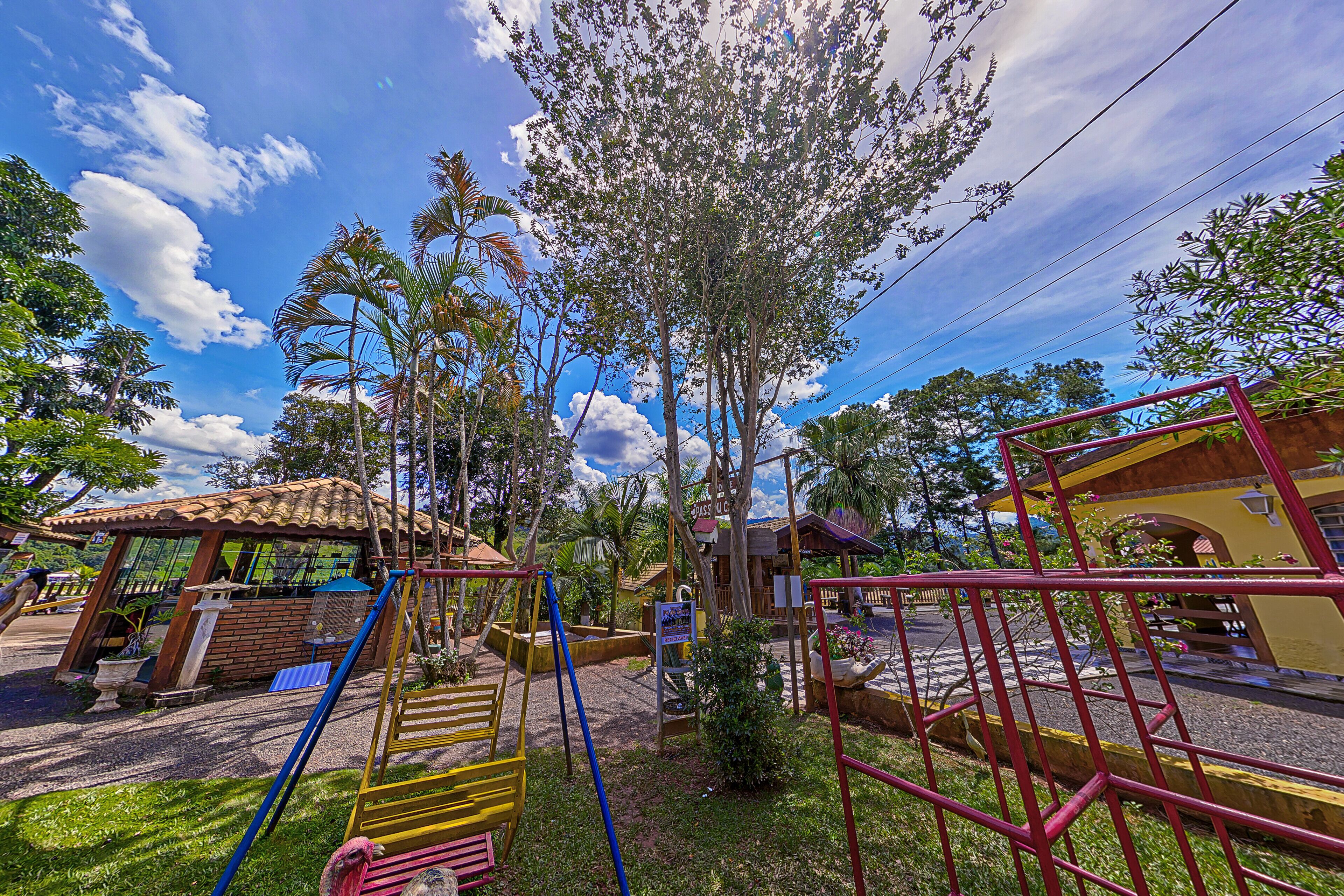 A playground with swings and slides, surrounded by trees and a building with a tiled roof.