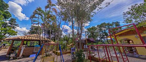 A playground with swings and slides, surrounded by trees and a building with a tiled roof.