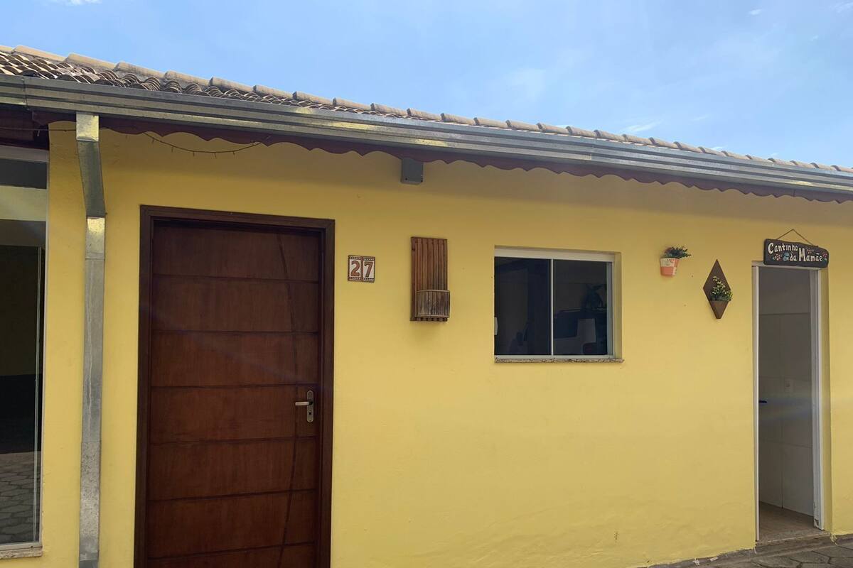 A yellow building with a brown door, a small window, and a sign that reads "Cantinho da Mamãe."