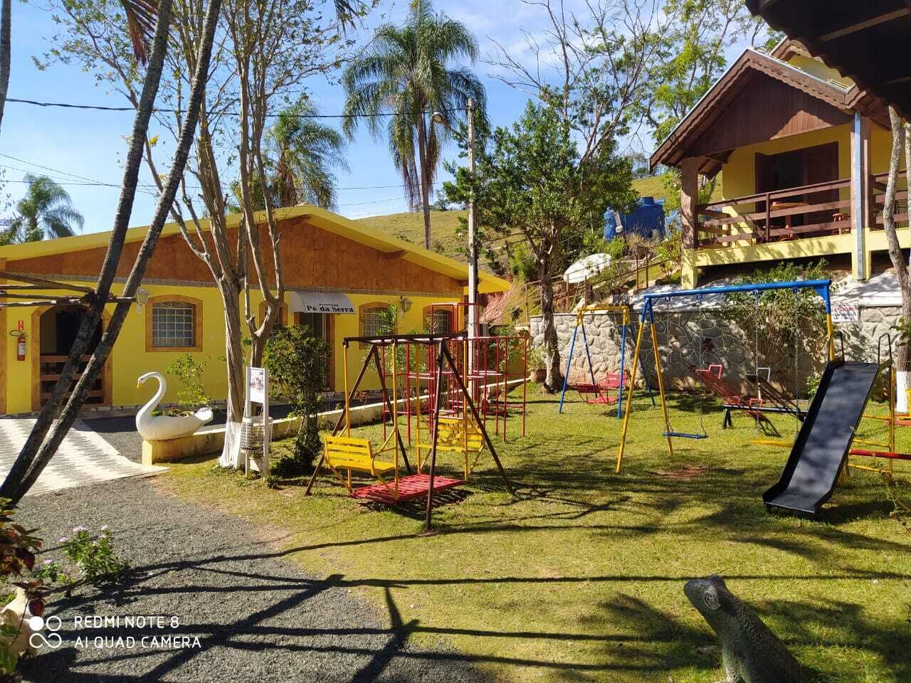 A playground with swings and a slide, surrounded by trees and a building with a yellow facade.