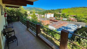 A balcony with a view of a town, a fire extinguisher, and a table with chairs. - Pousada Pé da Serra  (Lindoia)