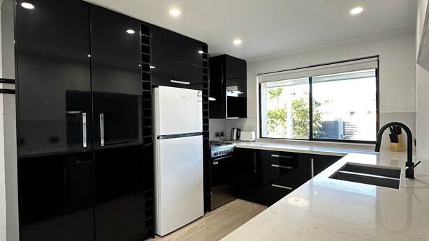 Una cocina moderna con armarios negros, un refrigerador blanco y un amplio ventanal que proporciona luz natural.
