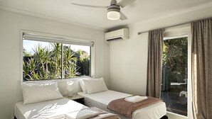 Un dormitorio con dos camas, ventilador de techo, equipo de aire acondicionado y un ventanal con cortinas.