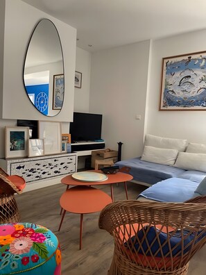 En moderne stue med sofa, fjernsyn, spisebord, fletstole og billedkunst på væggene.