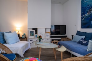 En moderne stue med sofa, fjernsyn, et lille bord og kunst på væggen.