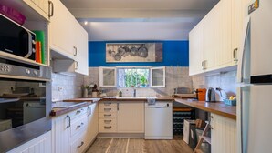 Une cuisine moderne avec des meubles blancs, un four à micro-ondes, un lave-vaisselle et une fenêtre donnant sur un espace verdoyant.