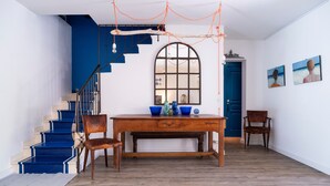 Un escalier aux marches bleues, une table en bois avec des chaises et une grande fenêtre en arc de cercle.
