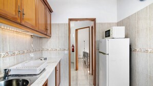 Une cuisine avec des meubles de rangement en bois, un évier blanc, un four à micro-ondes et un réfrigérateur.