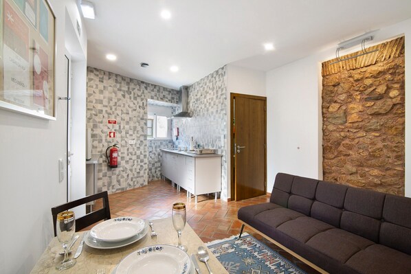 A modern living room with a sofa, a dining table set with plates, glasses, and cutlery, a kitchen in the background, and a stone accent wall.