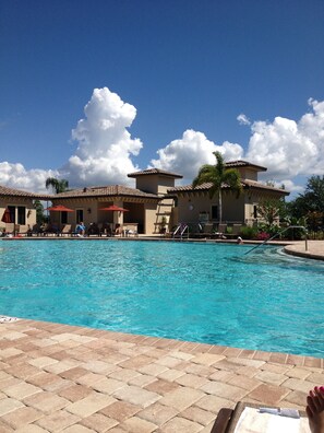 A pool area with lounge chairs and umbrellas, surrounded by buildings with a tiled roof.