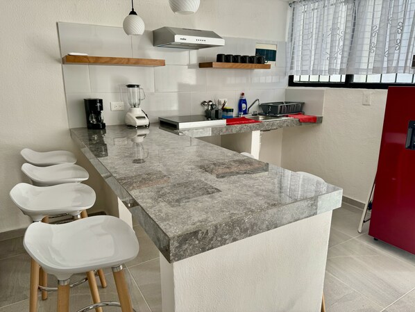 A modern kitchen with a marble countertop, built-in appliances, and a red refrigerator.
