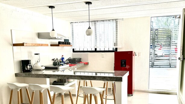 A modern kitchen with a central island, bar stools, and a red cabinet. - Depa Lunero, 5 minutes walking from the beach! (Cancún)