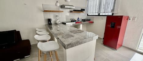 A modern kitchen with a marble countertop, wooden stools, a red refrigerator, and a built-in oven.