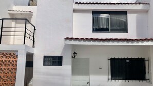 A white building with a white door, a window with a curtain, and a balcony with a railing. - Depa Lunero, 5 minutes walking from the beach! (Cancún)