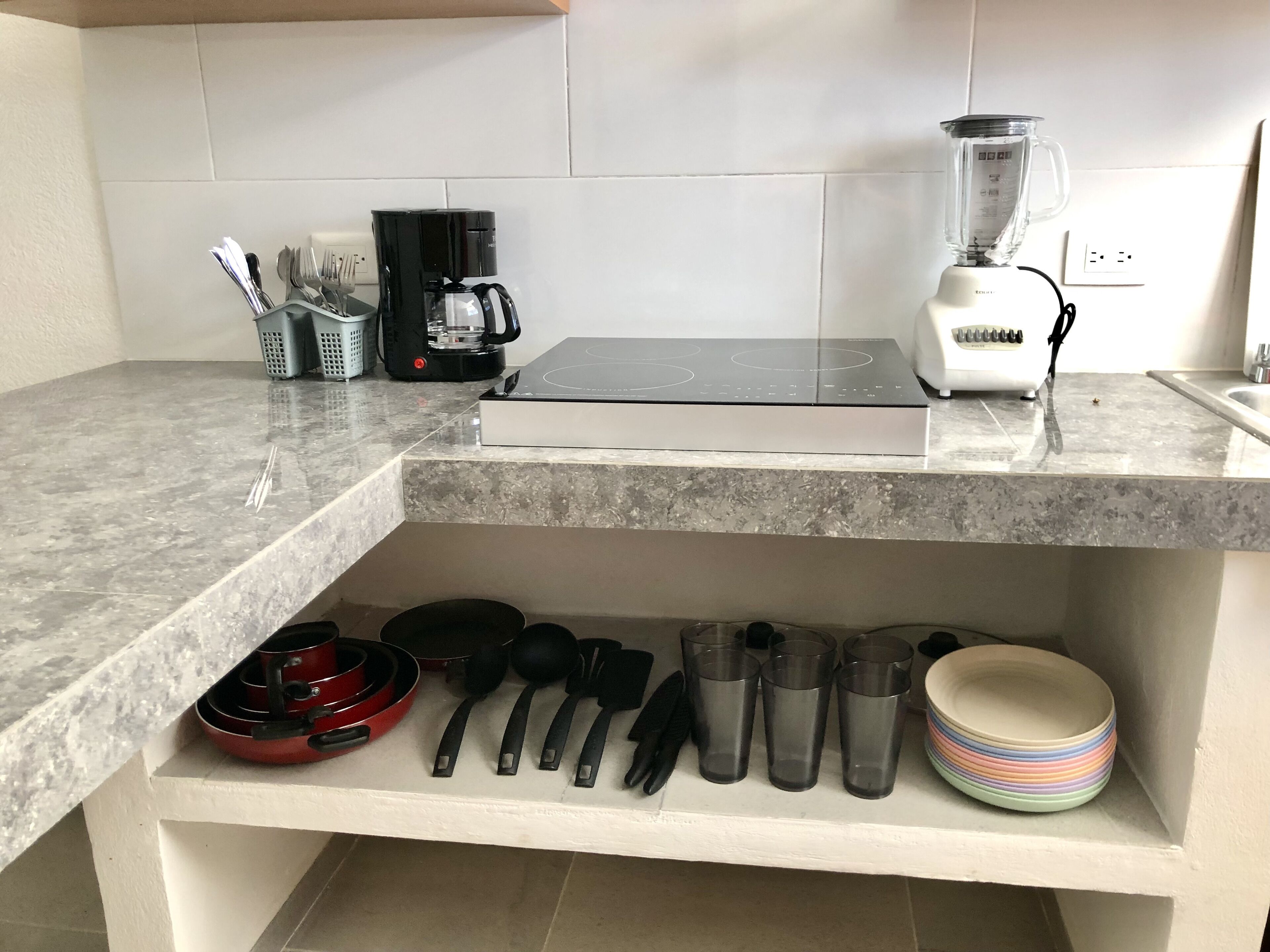 A kitchen with a countertop, a coffee maker, a blender, and various utensils.