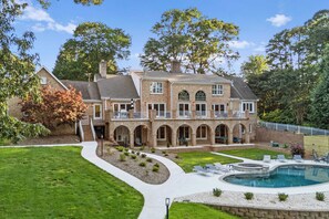 A large brick house with a swimming pool, multiple balconies, and a well-maintained lawn.