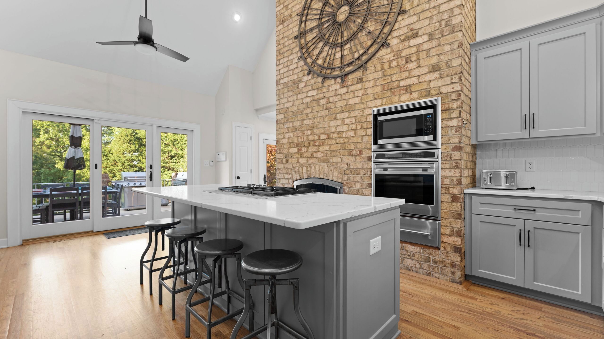 Een moderne keuken met een centraal eiland, barkrukken, een accentmuur van baksteen, en uitzicht door de glazen deuren.