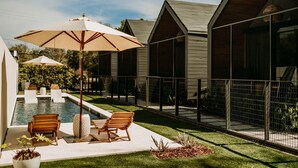 Ein Poolbereich mit Liegestühlen und einem großen Sonnenschirm, umgeben von einer eingezäunten Terrasse mit mehreren Zimmern.