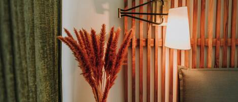 A room with a wooden slat wall, a clear glass vase with dried pampas grass, and a modern wall-mounted lamp.