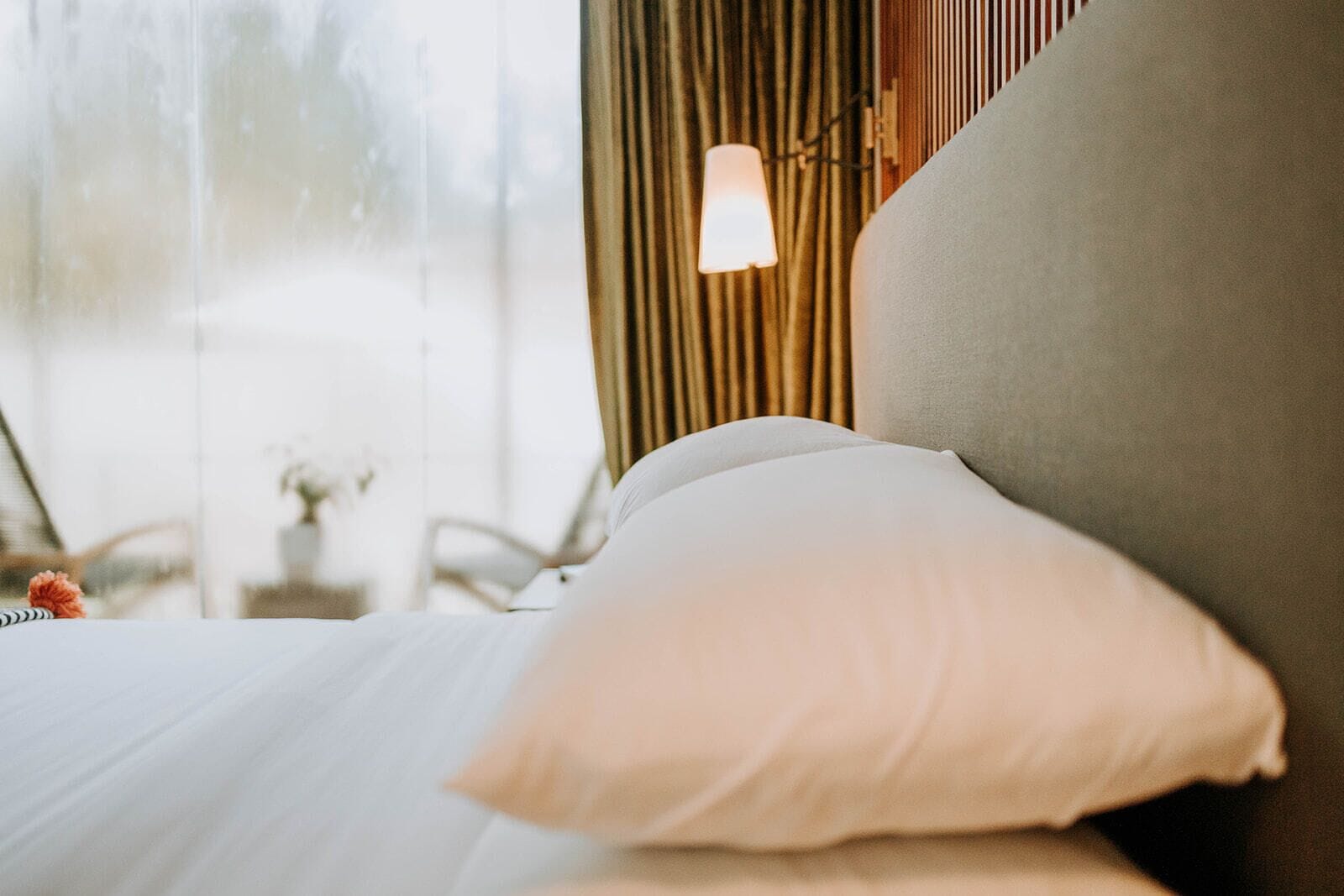 Un lit avec un oreiller blanc et une tête de lit grise dans une chambre d’hôtel.