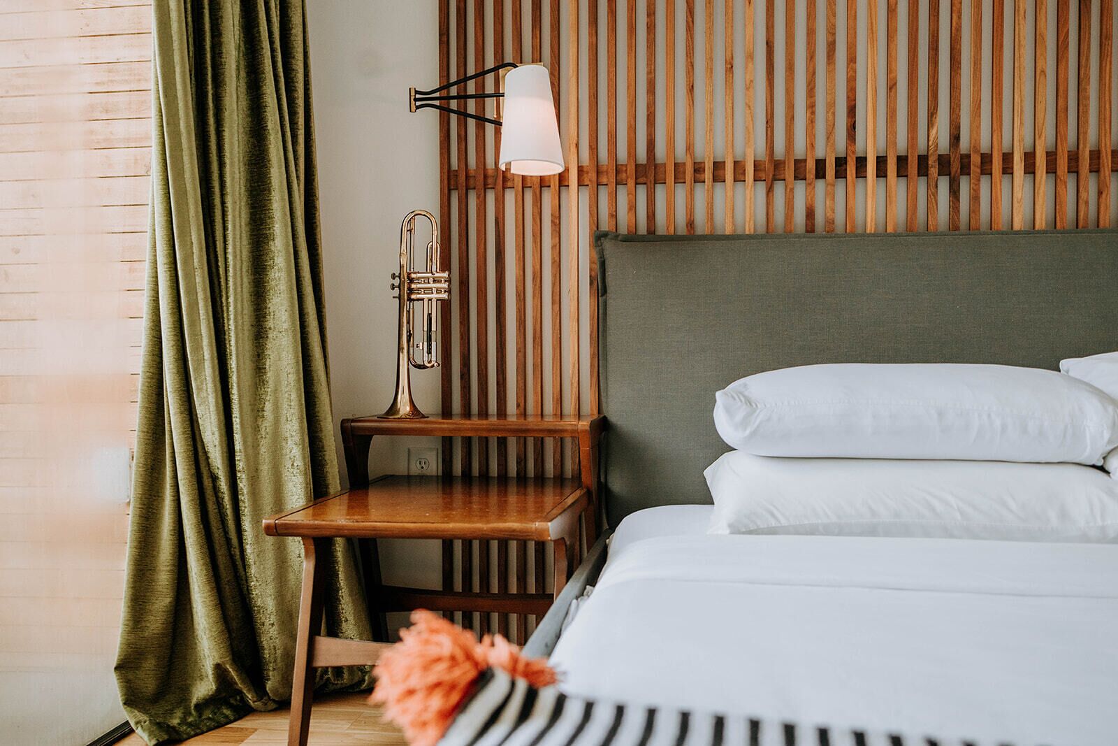 A neatly arranged hotel room with a bed, a bedside table, a lamp, and a curtain.