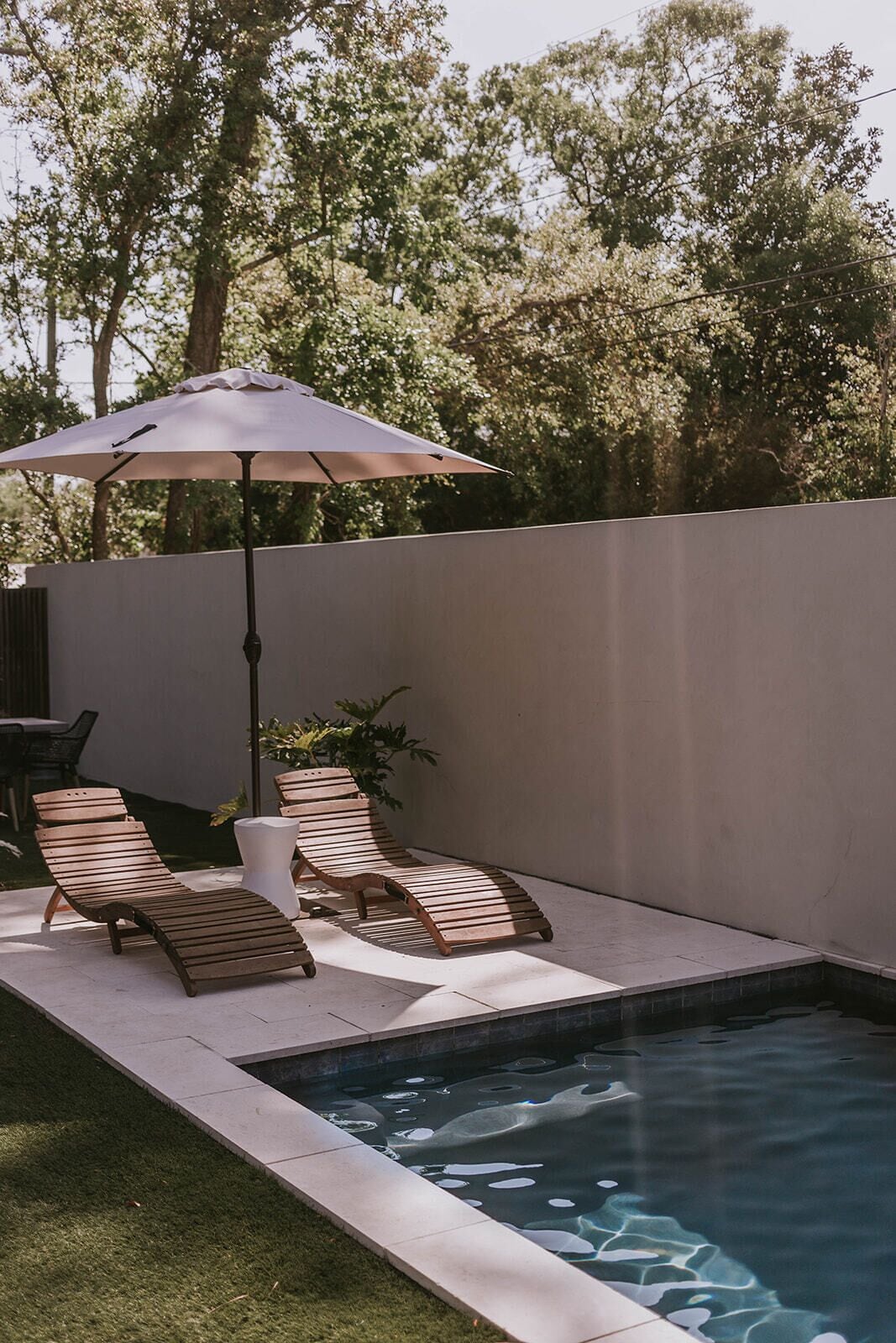 A swimming pool with two wooden lounge chairs and a white umbrella.