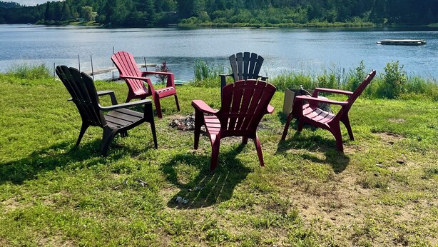 Näkymä järvelle, jossa on Adirondack-tyylisiä puutarhatuoleja ja pöytä, ja kaiken ympärillä on vehreää kasvillisuutta ja kirkas taivas.