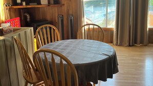 A dining area with a round table, wooden chairs, a television on the wall, and a view of a swimming pool through the window. - Peaceful Waterfront Cottage - Amazing Lake View - new SPA (Bowman)