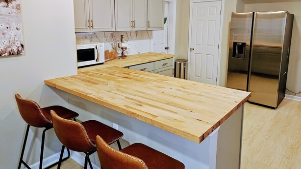 Eine moderne Küche mit weißen Schränken, einer Holz-Kochinsel mit Barhocker, einem Edelstahl-Kühlschrank und einer Mikrowelle.