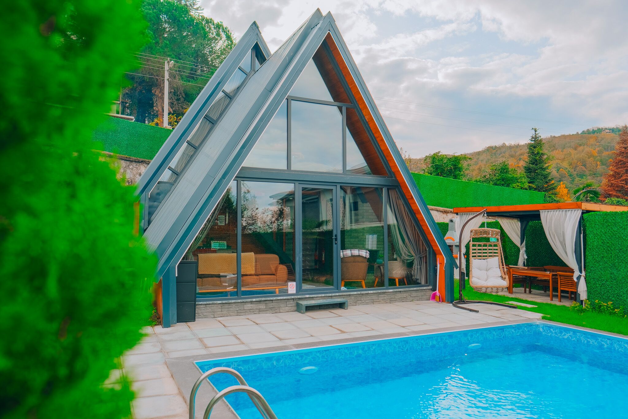 A modern house with a glass extension, a swimming pool, and a green lawn.