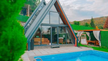 A modern house with a glass extension, a swimming pool, and a green lawn.