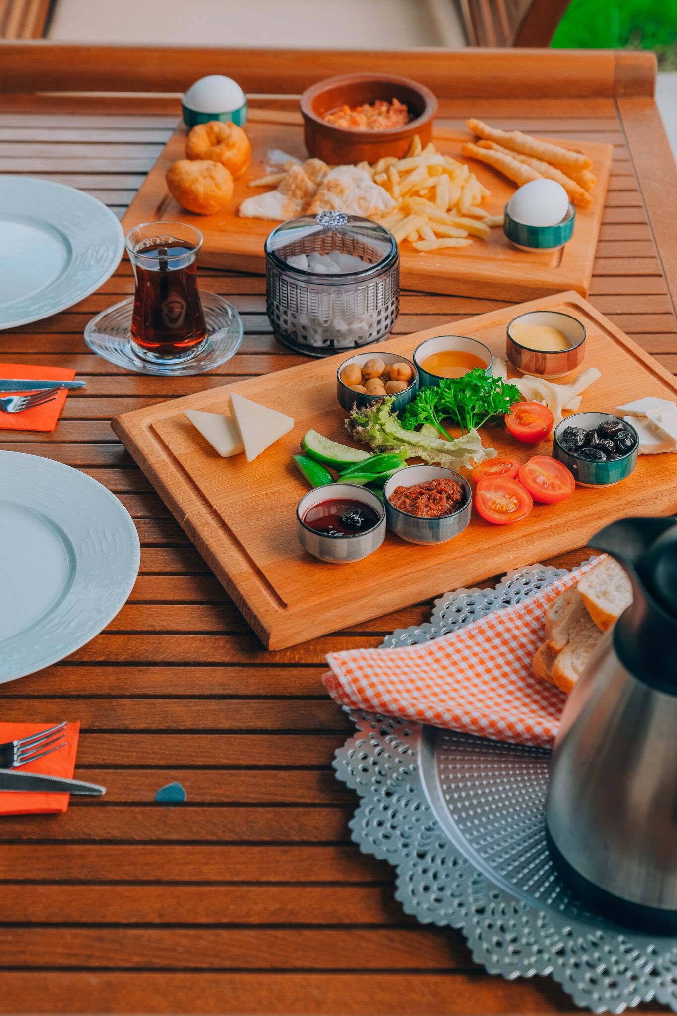 A wooden table with a variety of food items including bread, cheese, tomatoes, and olives, along with condiments and a glass of water.
