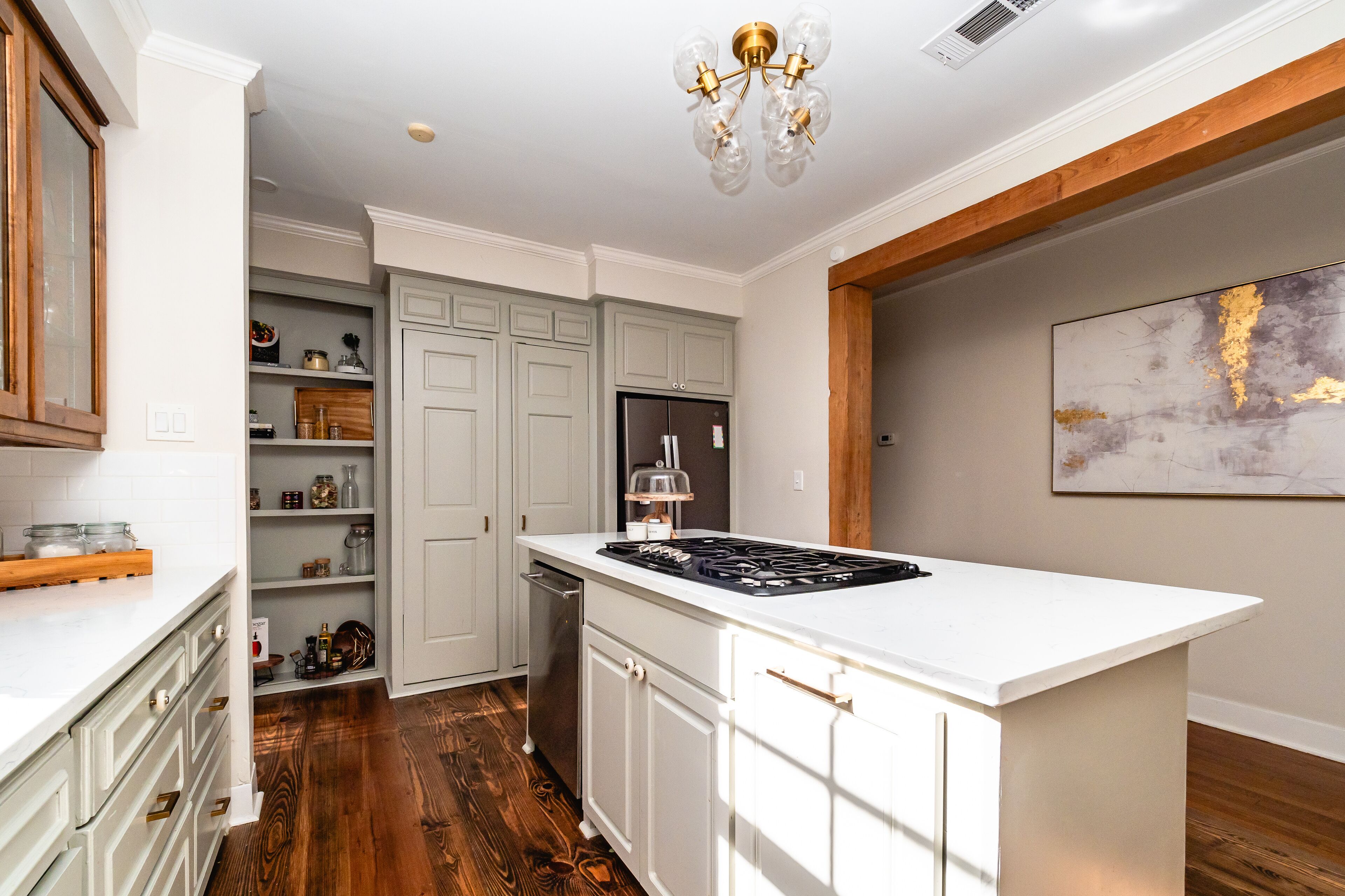 Une cuisine moderne avec des meubles blancs, une cuisinière encastrée et un plancher en bois.