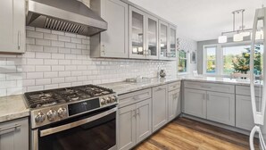 Une cuisine moderne avec des meubles gris, une cuisinière en acier inoxydable et une fenêtre donnant sur un paysage verdoyant.