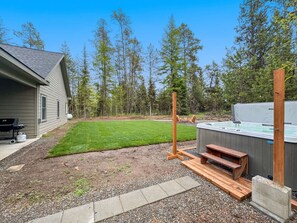 A backyard with a hot tub, wooden deck, and a house.