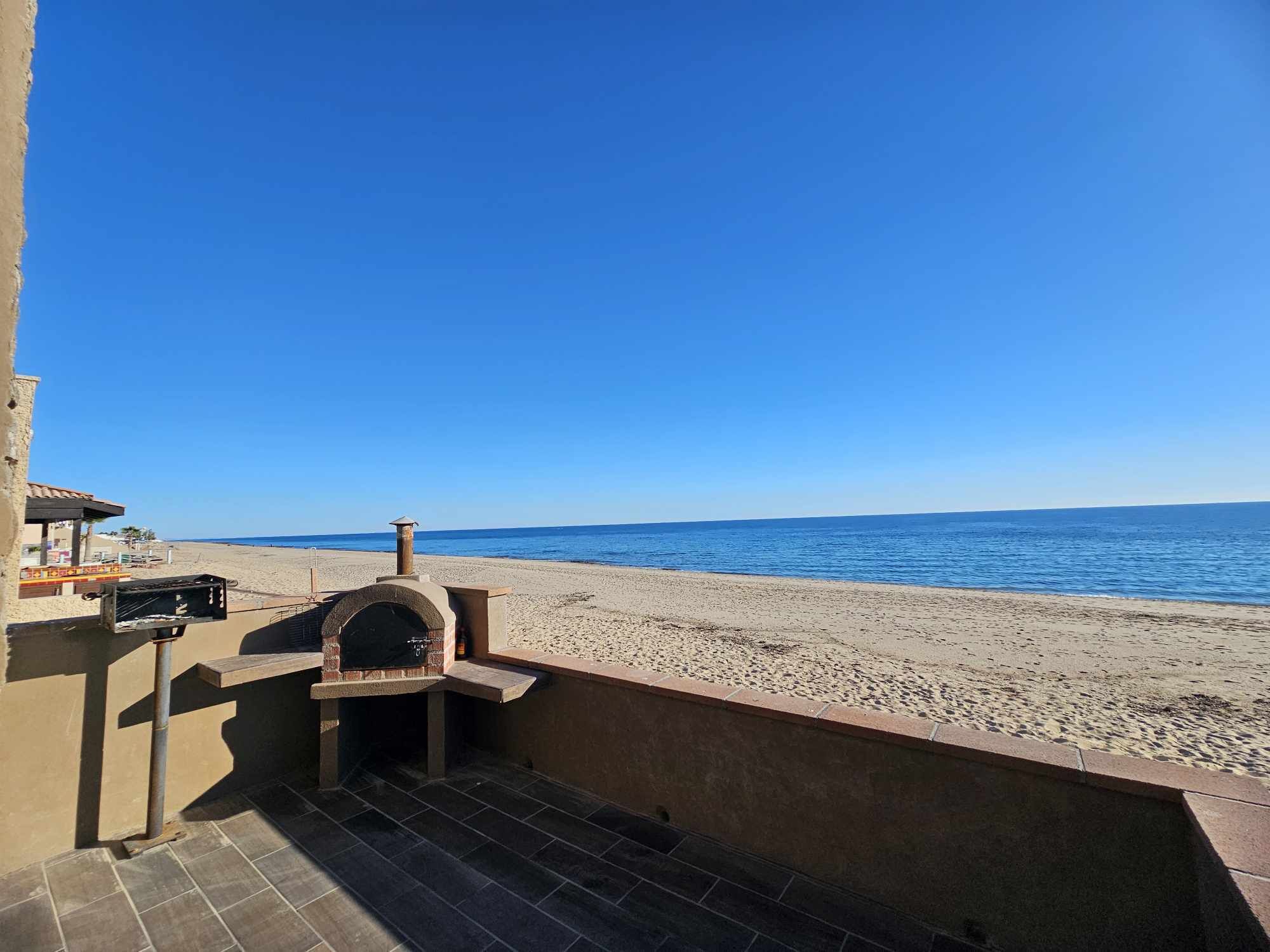En patio ved stranden med udendørs pizzaovn, flisegulv og havudsigt.