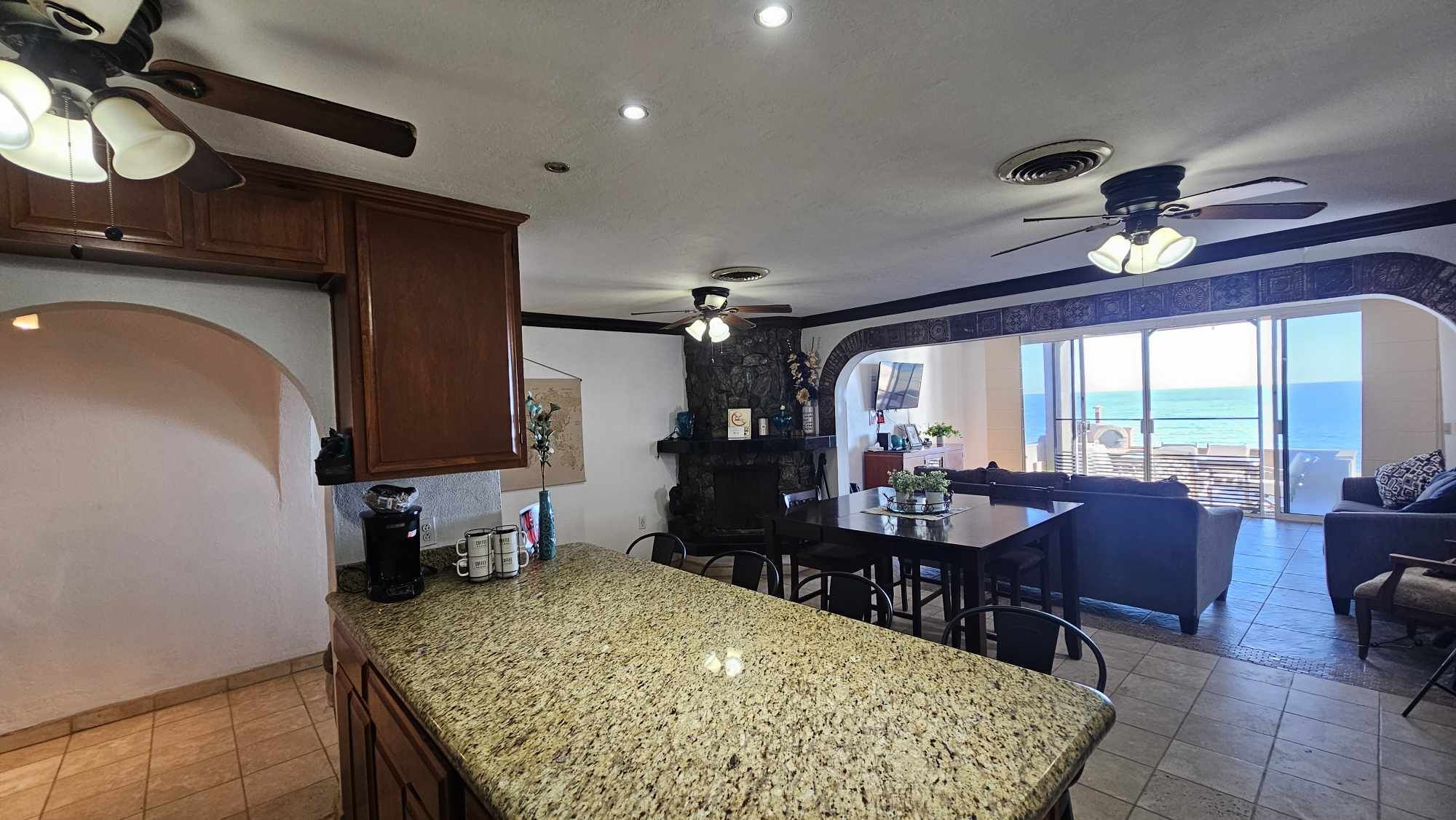 A kitchen with granite countertops, wooden cabinets, and a dining area with a view of the ocean.