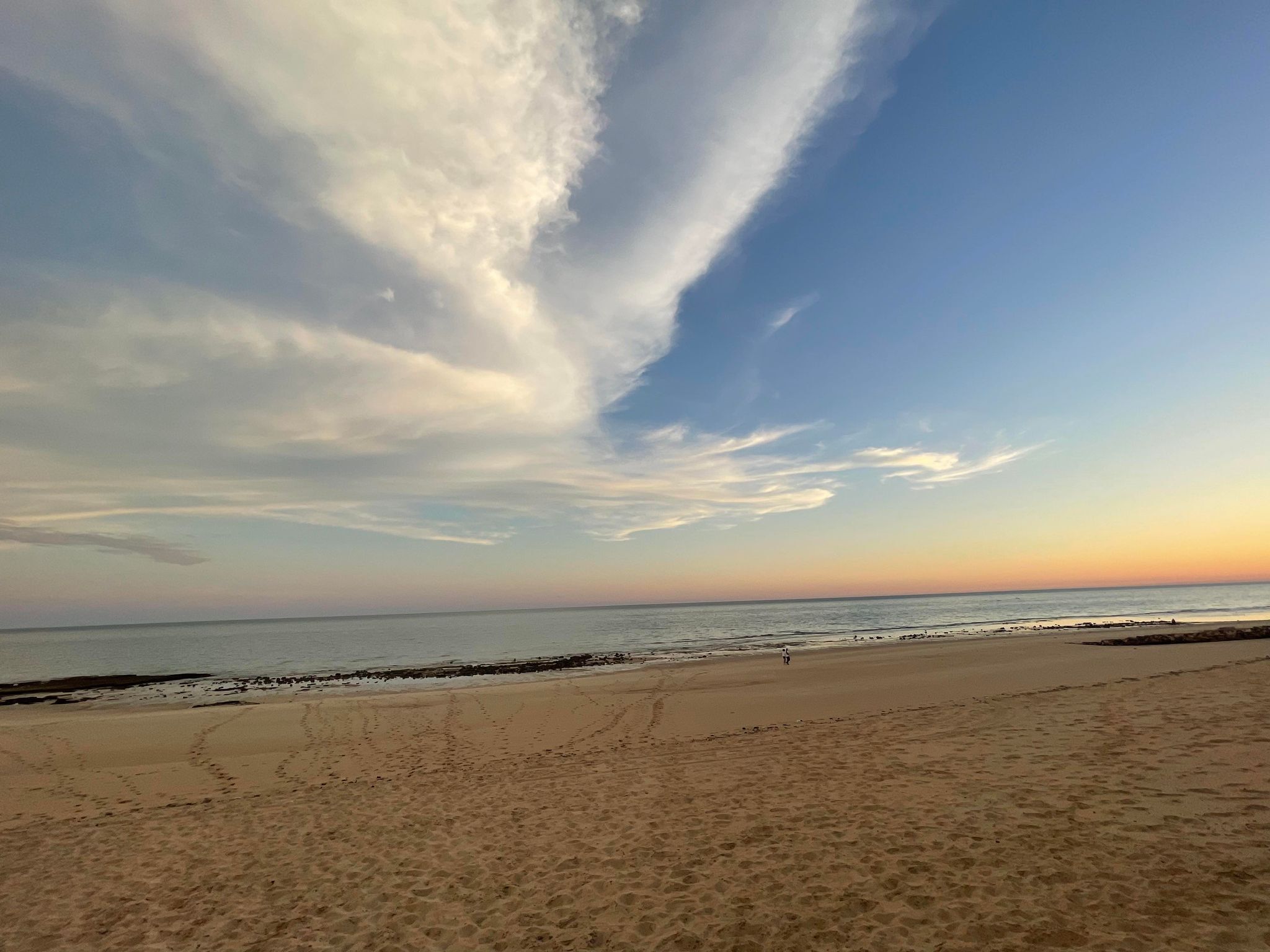 Una playa con una extensa zona arenosa y un cielo despejado con nubes.