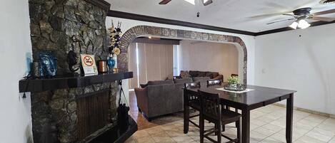 A living room with a stone fireplace, a dining table with chairs, a sofa, and a ceiling fan.